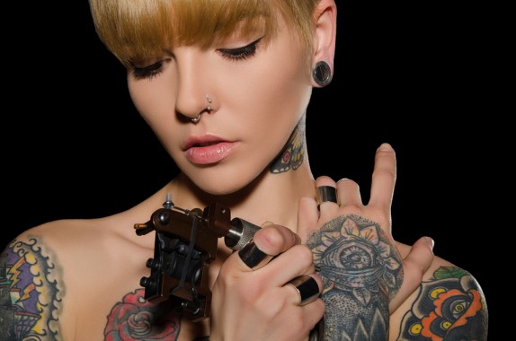 tattooed young woman with tattoo machine dark background